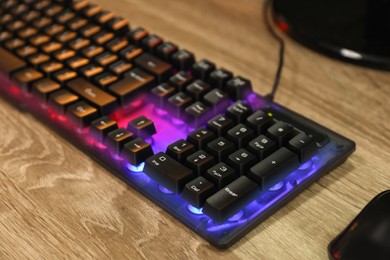 Modern RGB keyboard and mouse on wooden table indoors, closeup