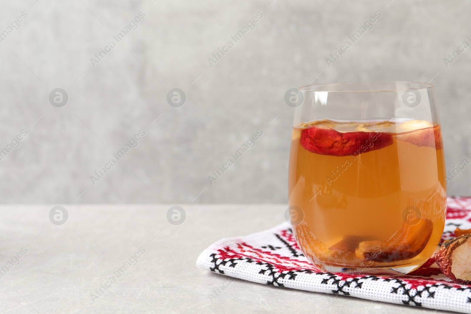 Photo of Delicious compote with dried apple slices in glass and rushnyk on light grey table, space for text