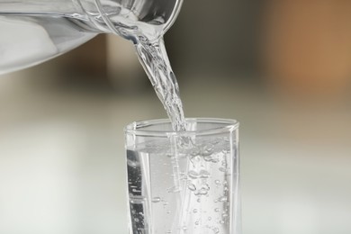 Pouring water from jug into glass on blurred background, closeup