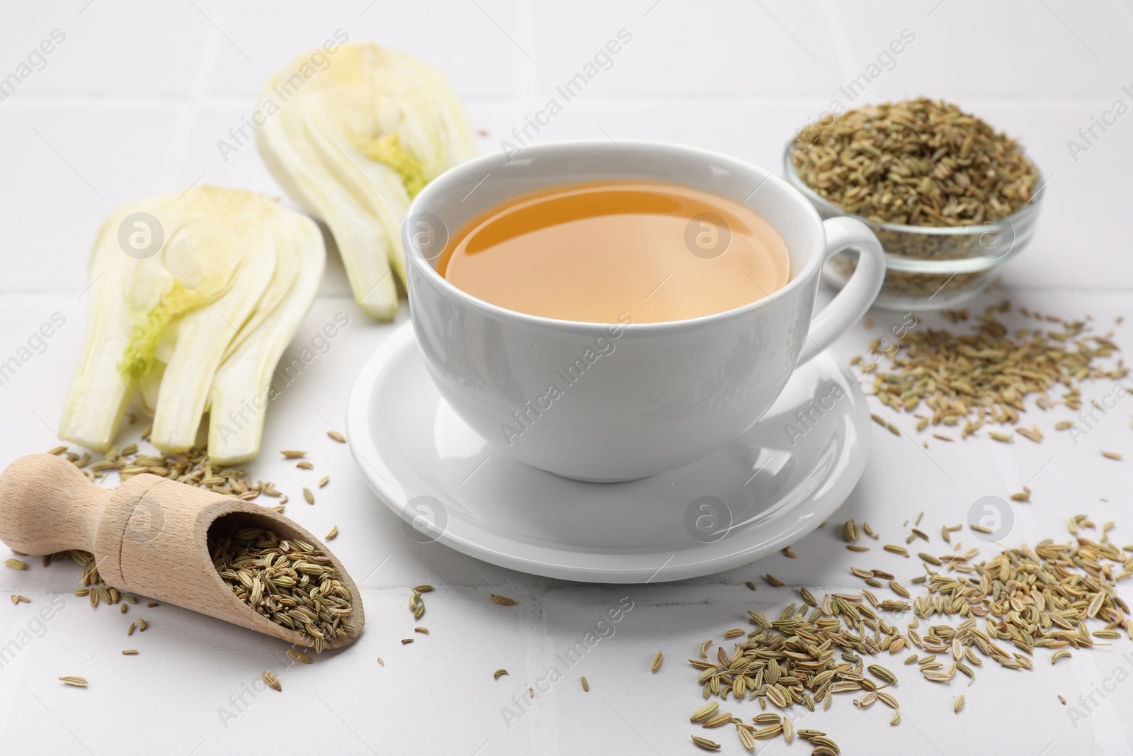 Photo of Fennel tea in cup, seeds and fresh vegetable on white tiled table, closeup