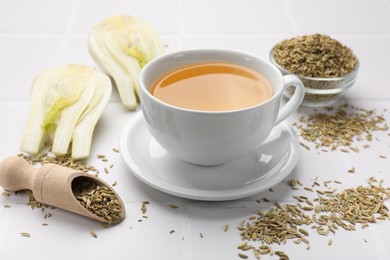 Fennel tea in cup, seeds and fresh vegetable on white tiled table, closeup