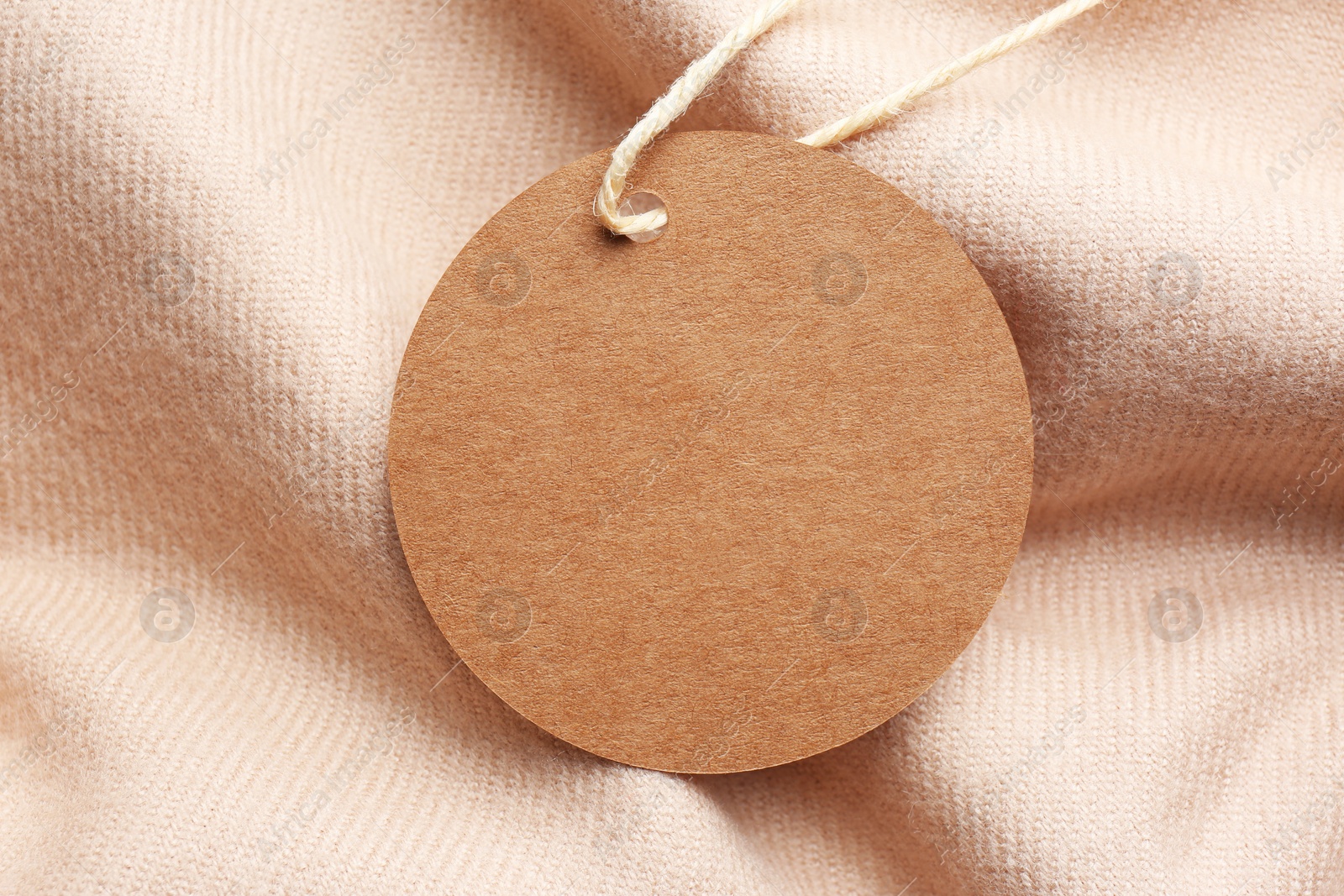 Photo of Circle shaped tag with space for text on beige fabric, top view