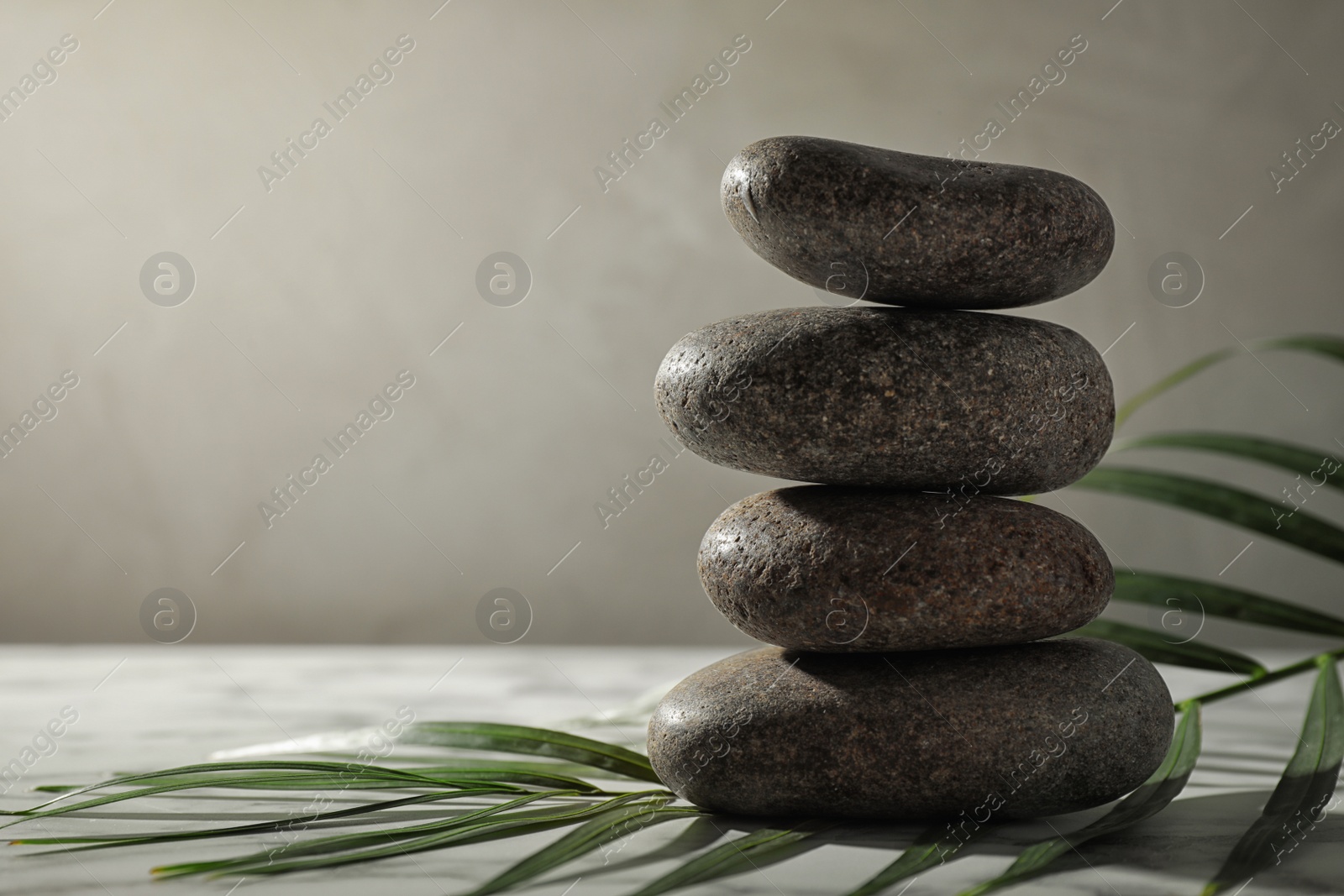 Photo of Stack of spa stones and palm leaf on grey table, space for text