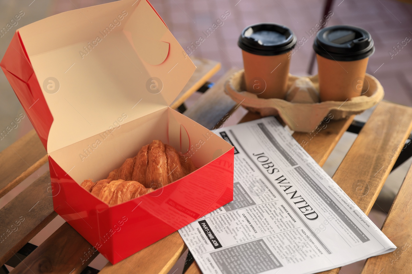 Photo of Tasty croissants, newspaper and cups of coffee on wooden table outdoors