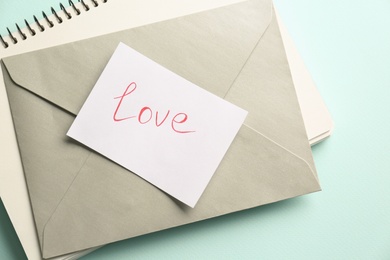 Photo of Card with handwritten word love, envelope and notebook on turquoise background, top view