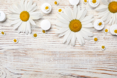 Flat lay composition with chamomile flowers and cosmetic products on white wooden table, space for text