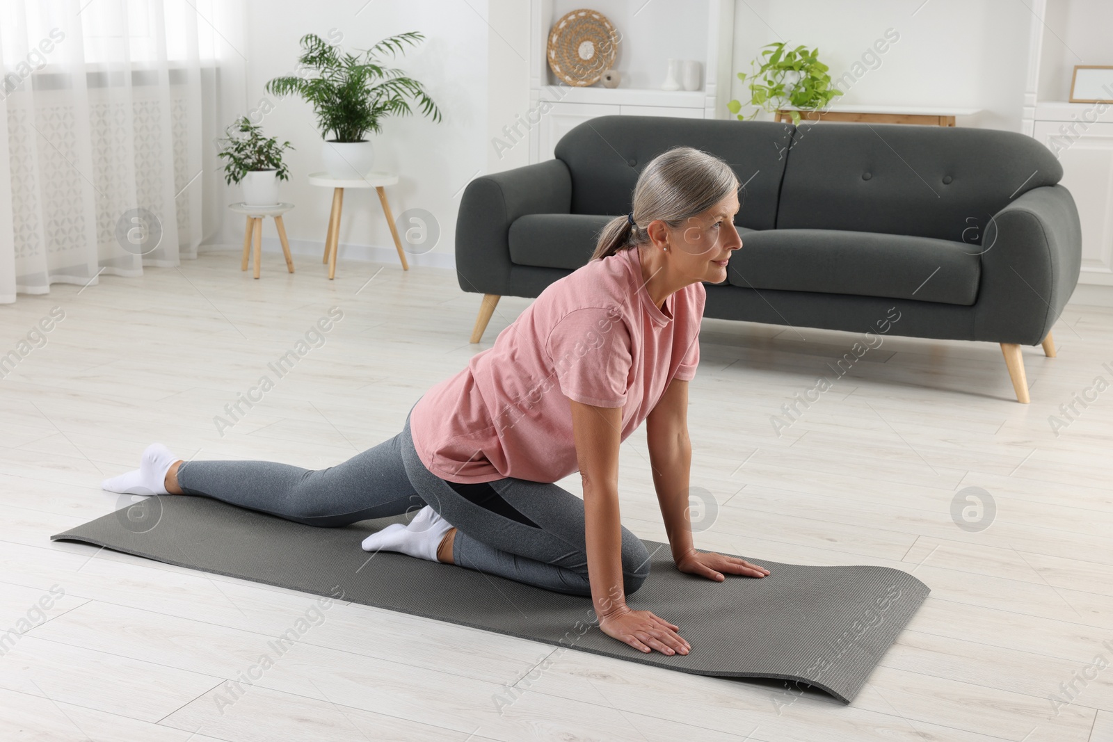 Photo of Senior woman in sportswear stretching on fitness mat at home