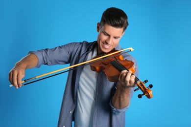 Happy man playing violin on light blue background