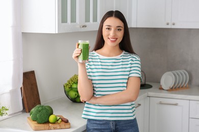 Photo of Beautiful young woman holding glass with tasty smoothie in kitchen