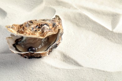 Photo of Open oyster with black pearl on sand, space for text