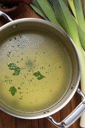 Pot with tasty bouillon and celery on wooden table, flat lay