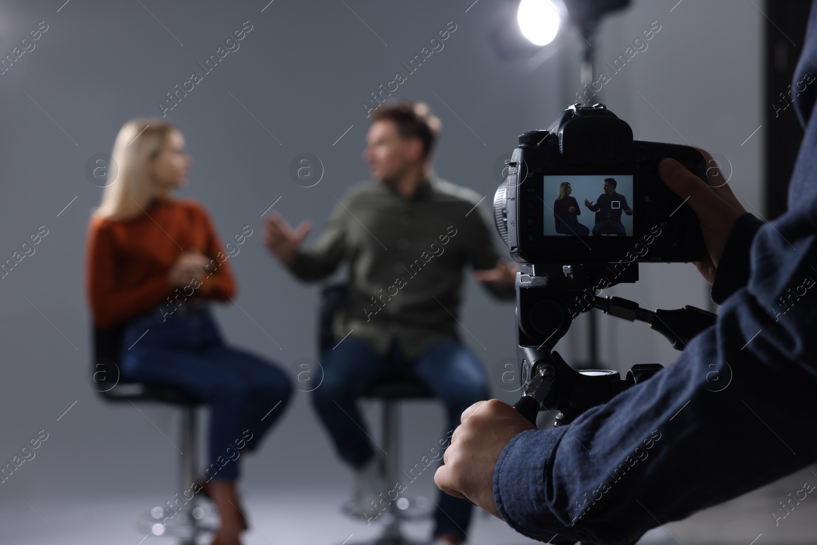 Photo of Casting call. Man and woman performing while camera operator filming them against grey background in studio, selective focus