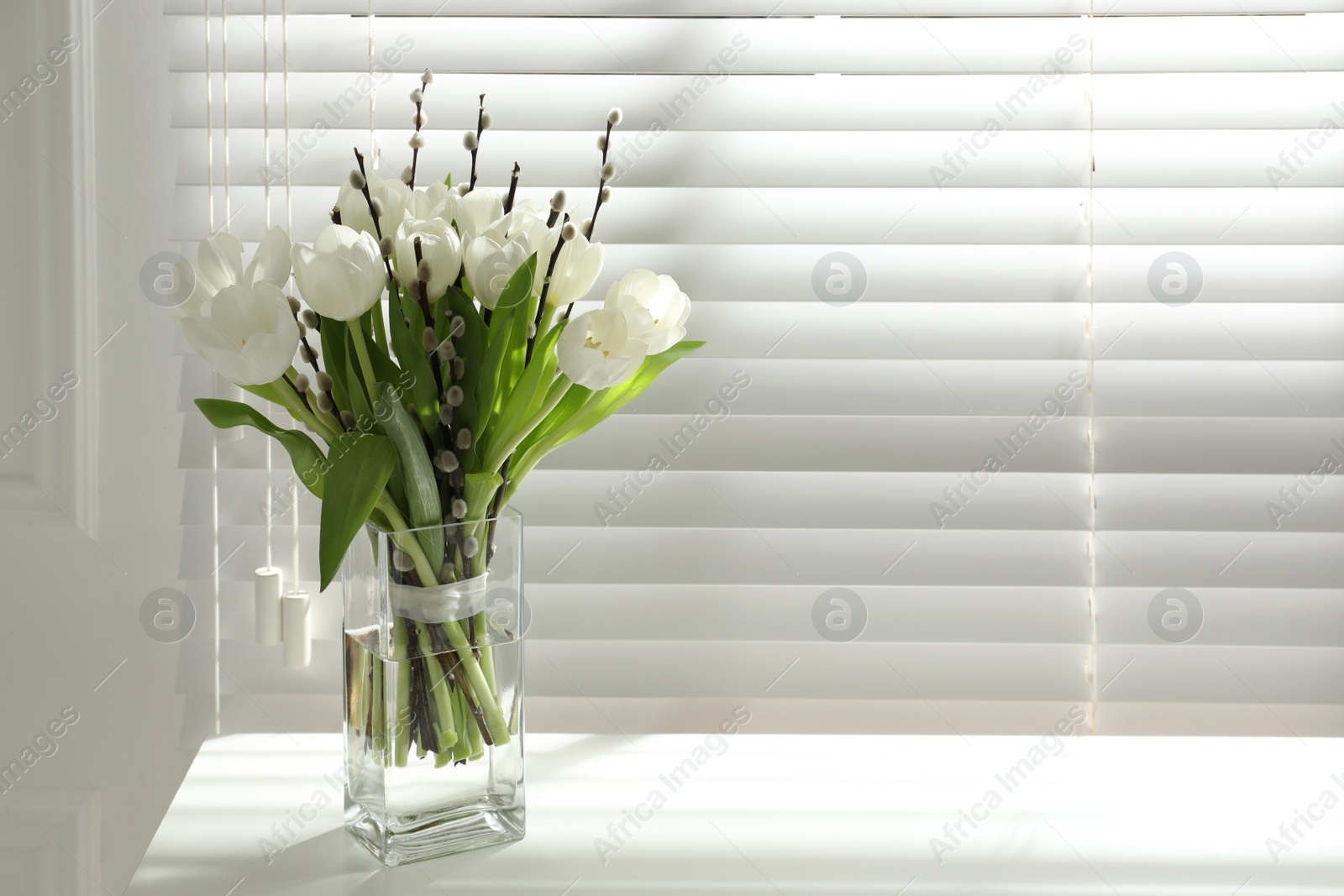 Photo of Beautiful bouquet of willow branches and tulips in vase near window, space for text