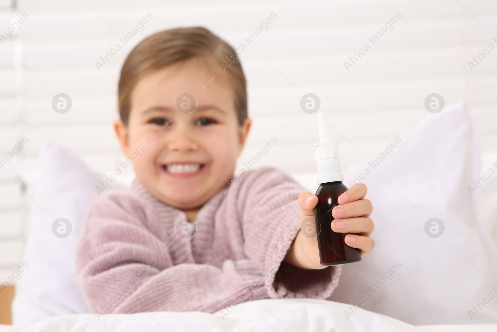 Photo of Cute little girl showing nasal spray indoors, focus on hand