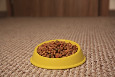 Photo of Dry pet food in feeding bowl on soft carpet indoors