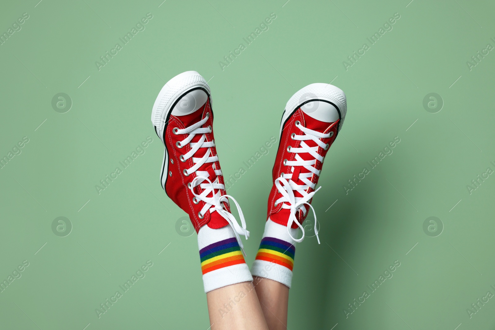 Photo of Woman in stylish gumshoes on pale green background, closeup