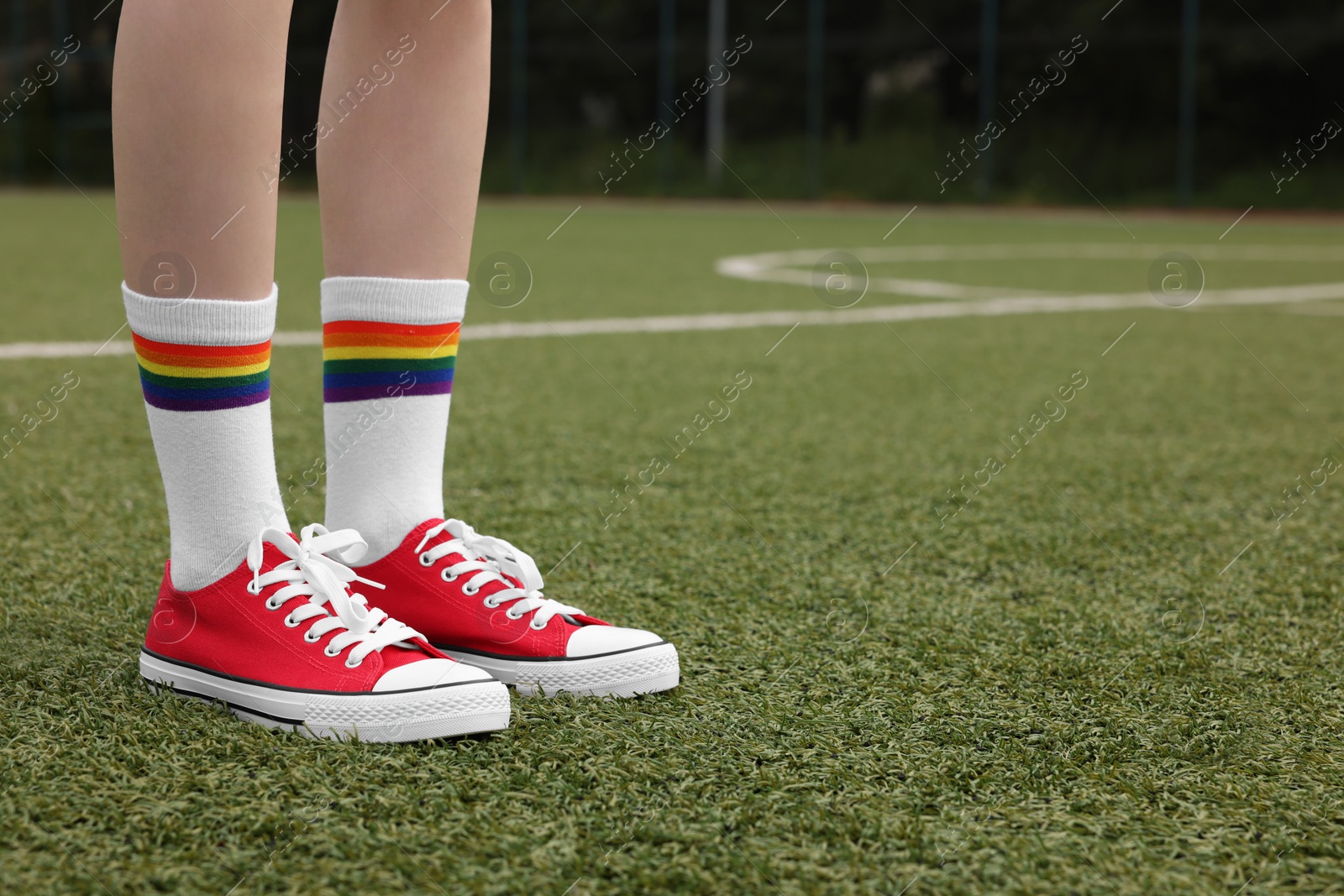 Photo of Woman wearing red classic old school sneakers on green court outdoors, closeup. Space for text