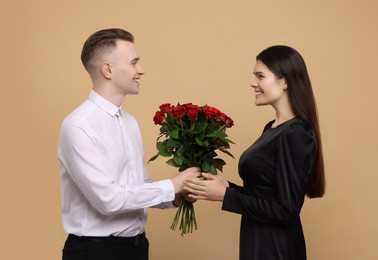 Photo of Boyfriend presenting beautiful bouquet roses to his girlfriend on beige background. Valentine's day celebration