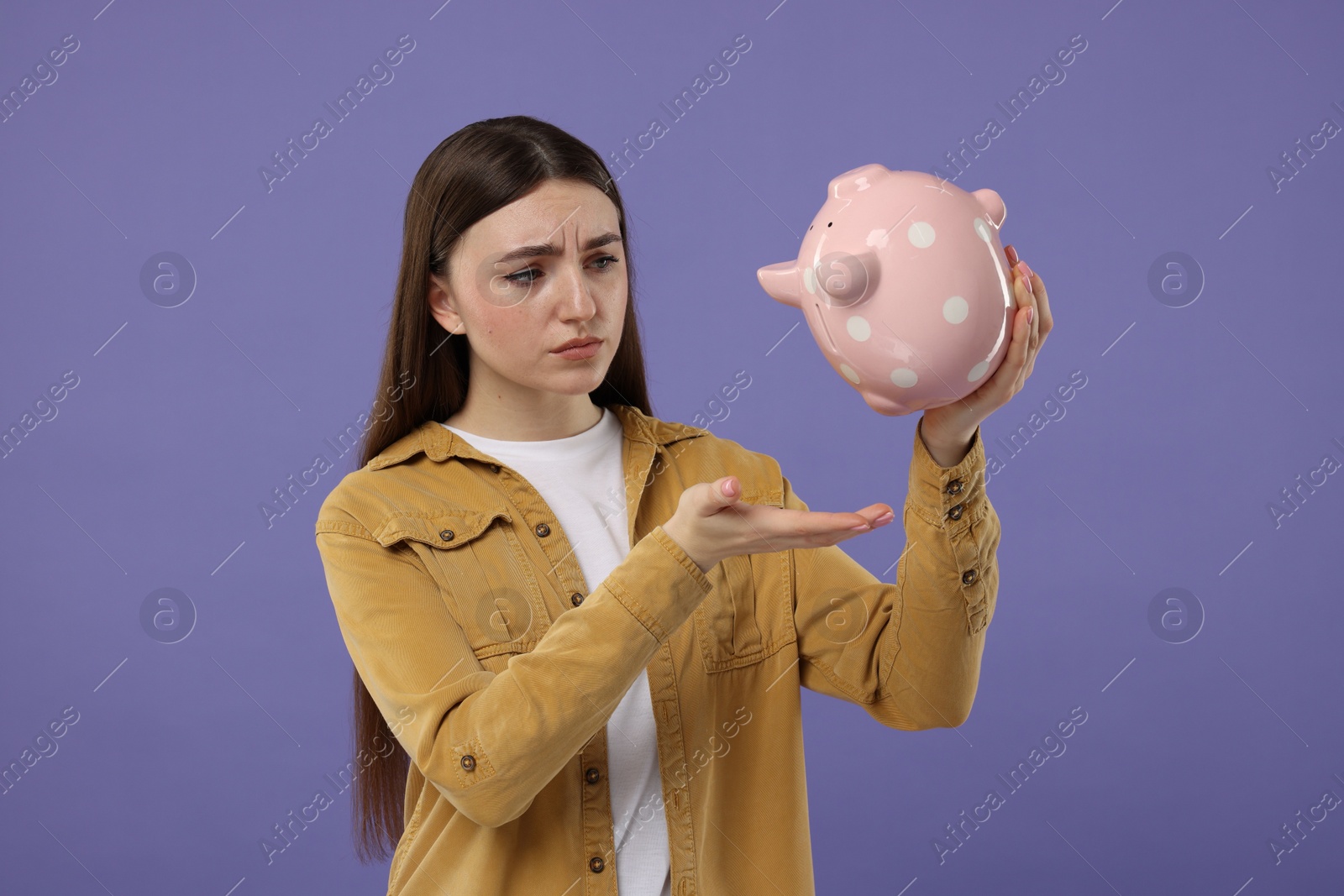 Photo of Sad woman with piggy bank on purple background