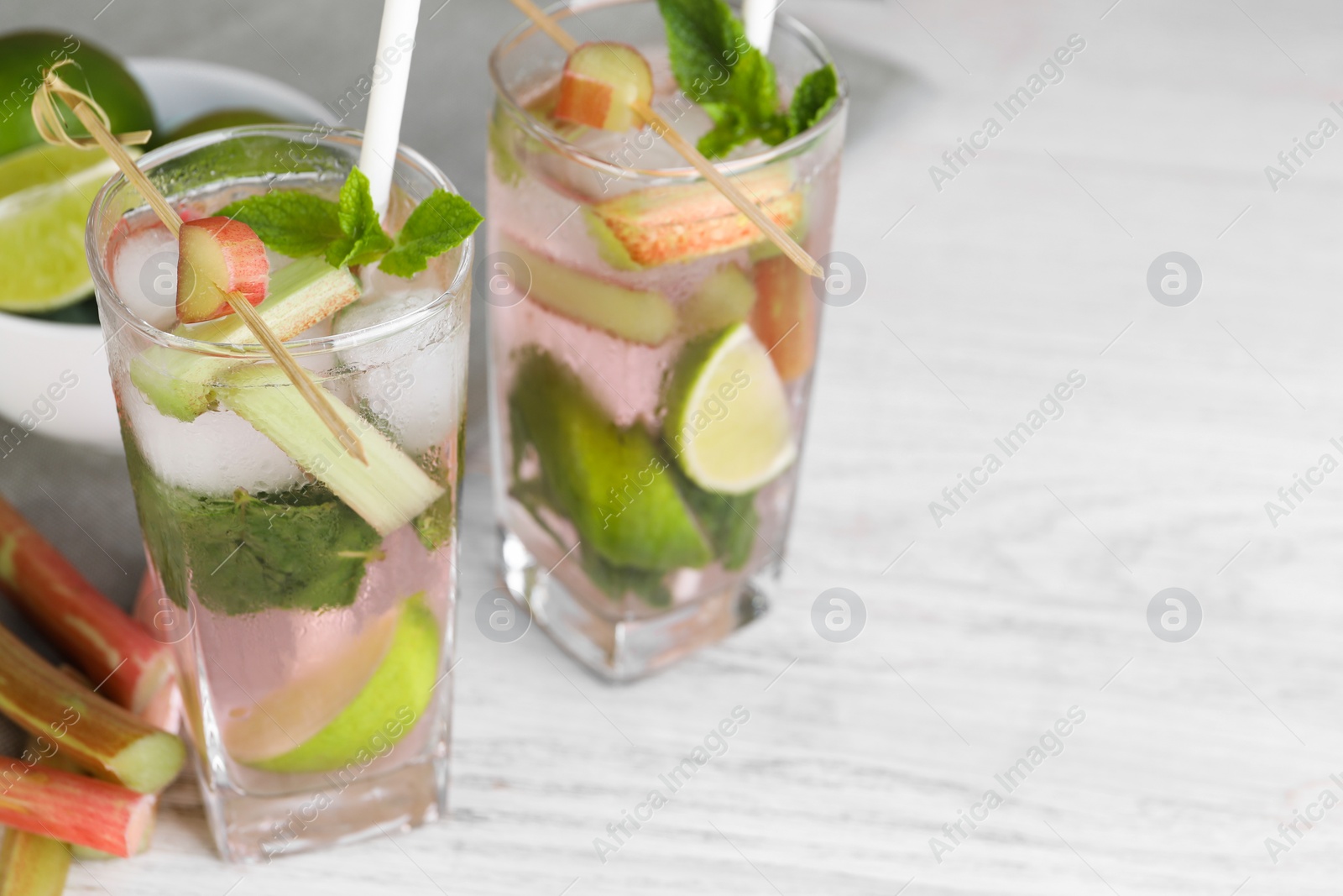 Photo of Tasty rhubarb cocktail with lime on white wooden table, space for text
