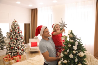 Father and little daughter decorating Christmas tree with star topper in room