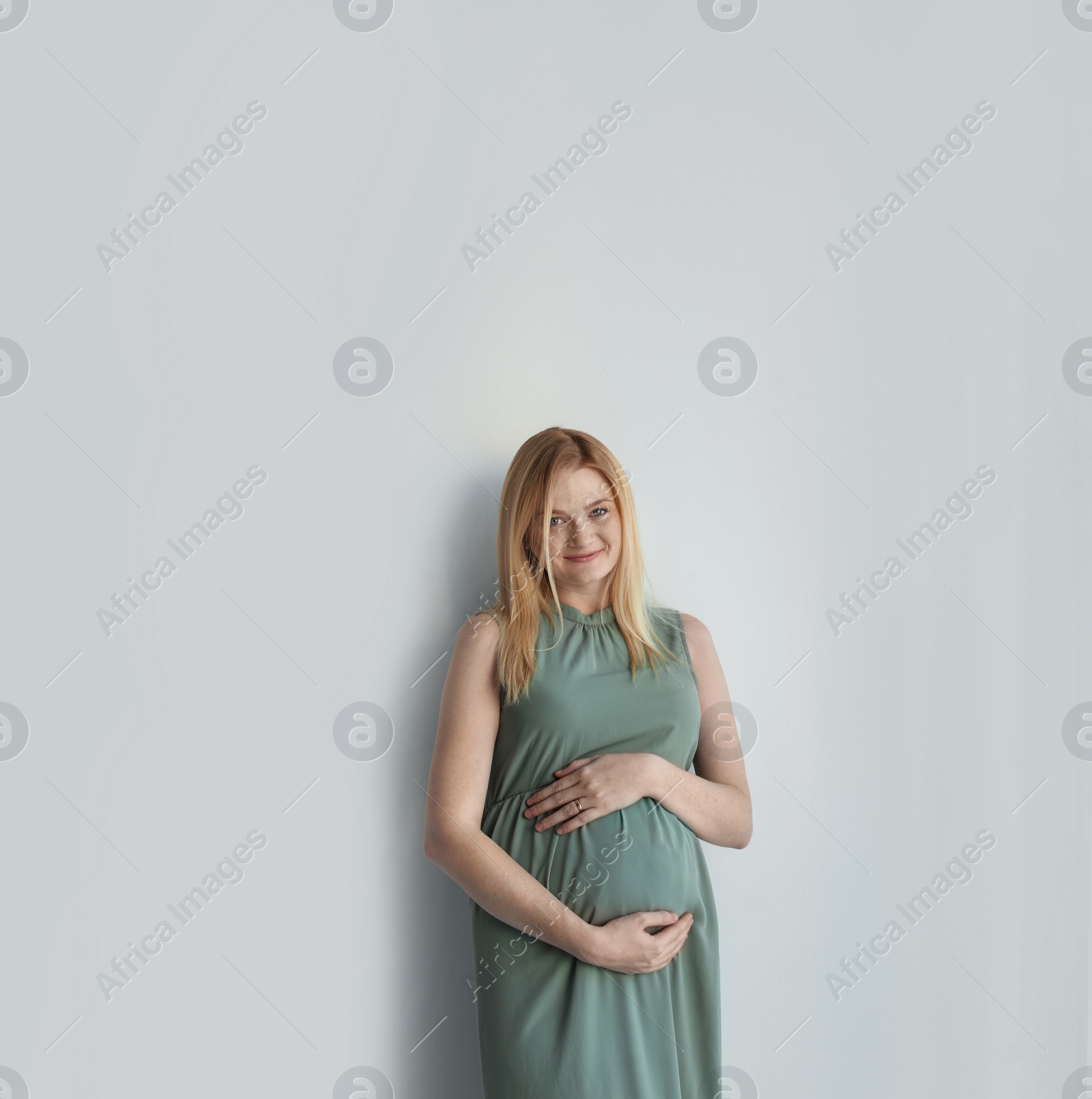 Photo of Young pregnant woman touching belly on light background