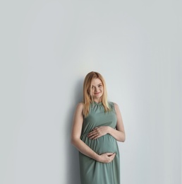 Photo of Young pregnant woman touching belly on light background