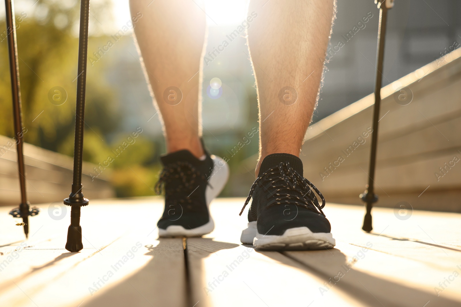 Photo of Man practicing Nordic walking with poles outdoors on sunny day, closeup