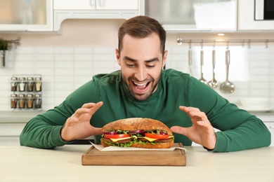 Photo of Young hungry man and tasty sandwich in kitchen