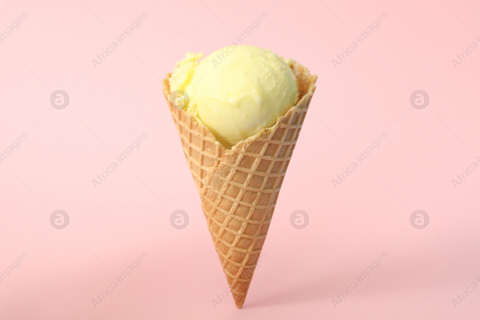 Photo of Delicious yellow ice cream in waffle cone on pink background