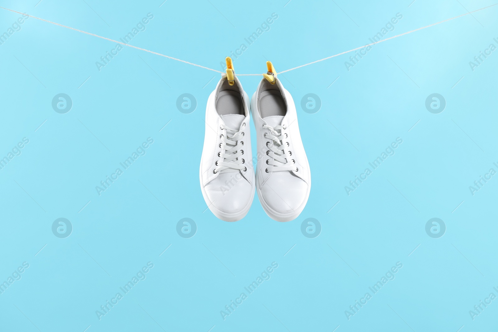 Photo of Stylish sneakers drying on washing line against light blue background