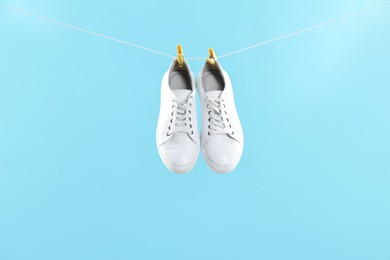 Stylish sneakers drying on washing line against light blue background