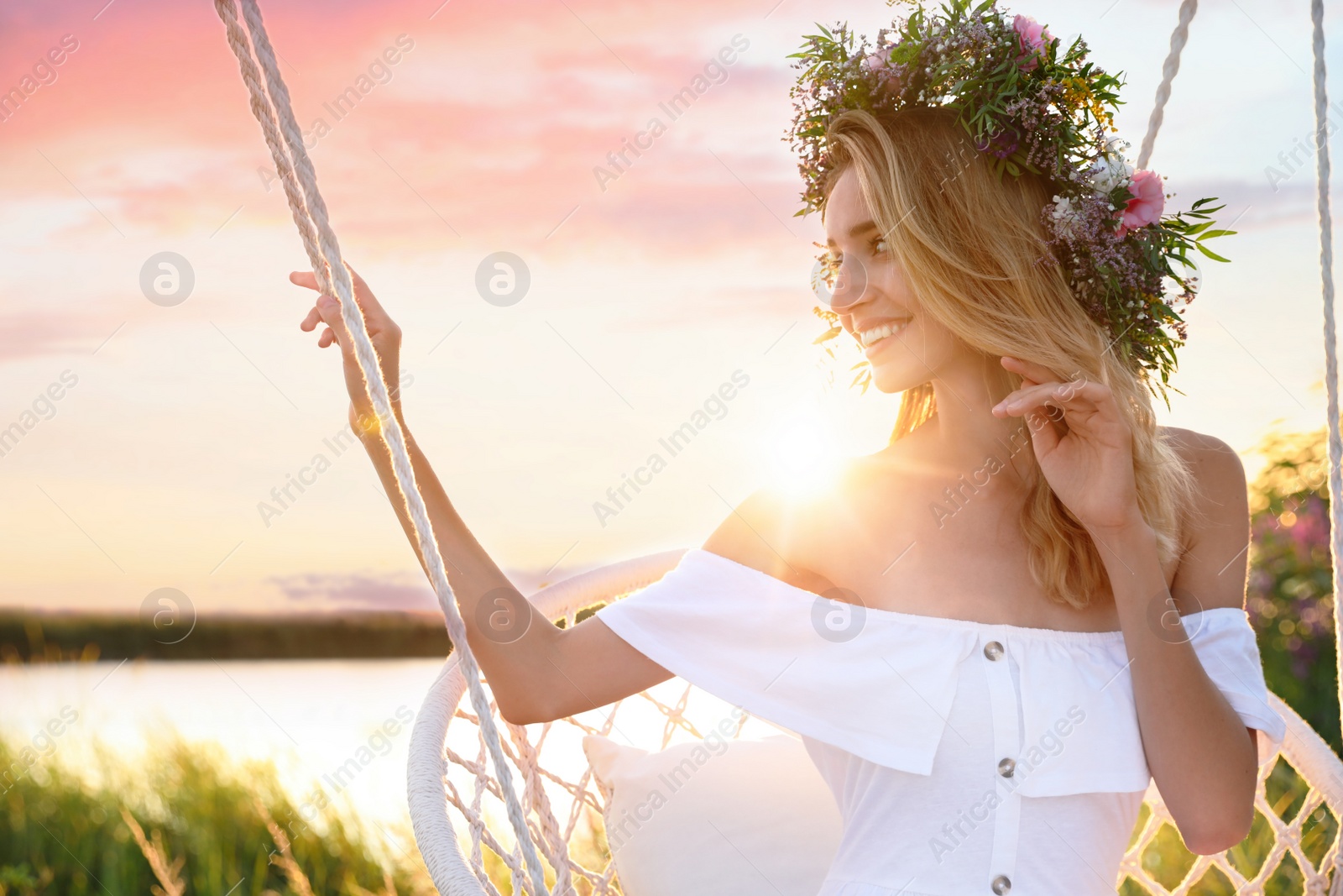 Photo of Young woman wearing wreath made of beautiful flowers on swing chair outdoors