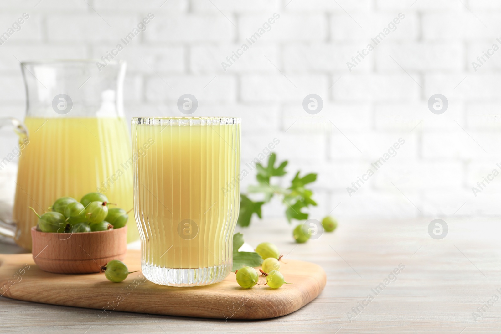 Photo of Tasty gooseberry juice and fresh berries on light wooden table. Space for text