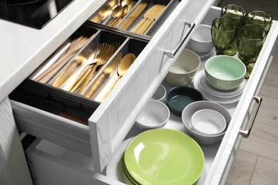 Photo of Ceramic dishware and cutlery in drawers indoors