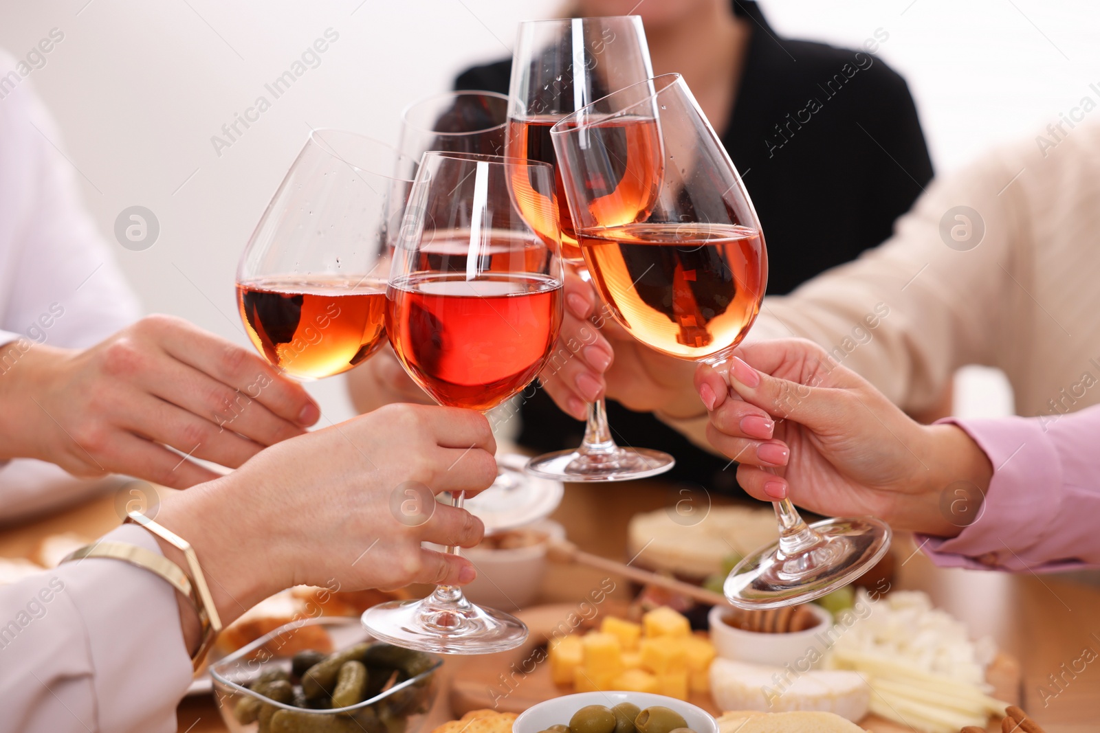 Photo of People clinking glasses with rose wine above table indoors, closeup