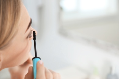 Photo of Young woman with eyelash loss problem applying mascara indoors