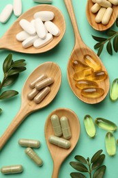 Photo of Different vitamin capsules in spoons and leaves on turquoise background, flat lay