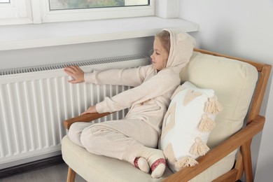 Little girl warming hands near heating radiator indoors