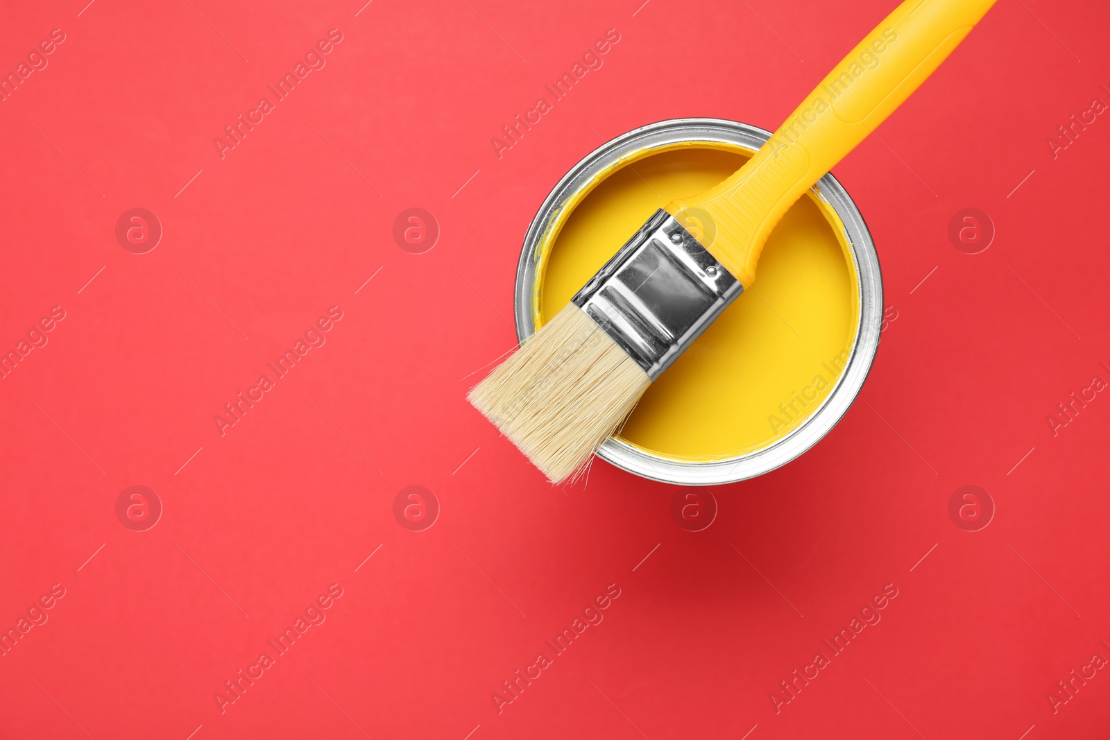 Photo of Can of yellow paint with brush on red background, top view. Space for text