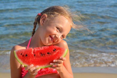 Photo of Cute little girl with slice of fresh juicy watermelon on beach, space for text