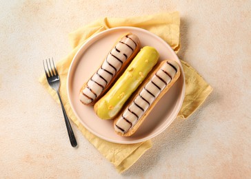 Different tasty glazed eclairs served on color textured table, top view