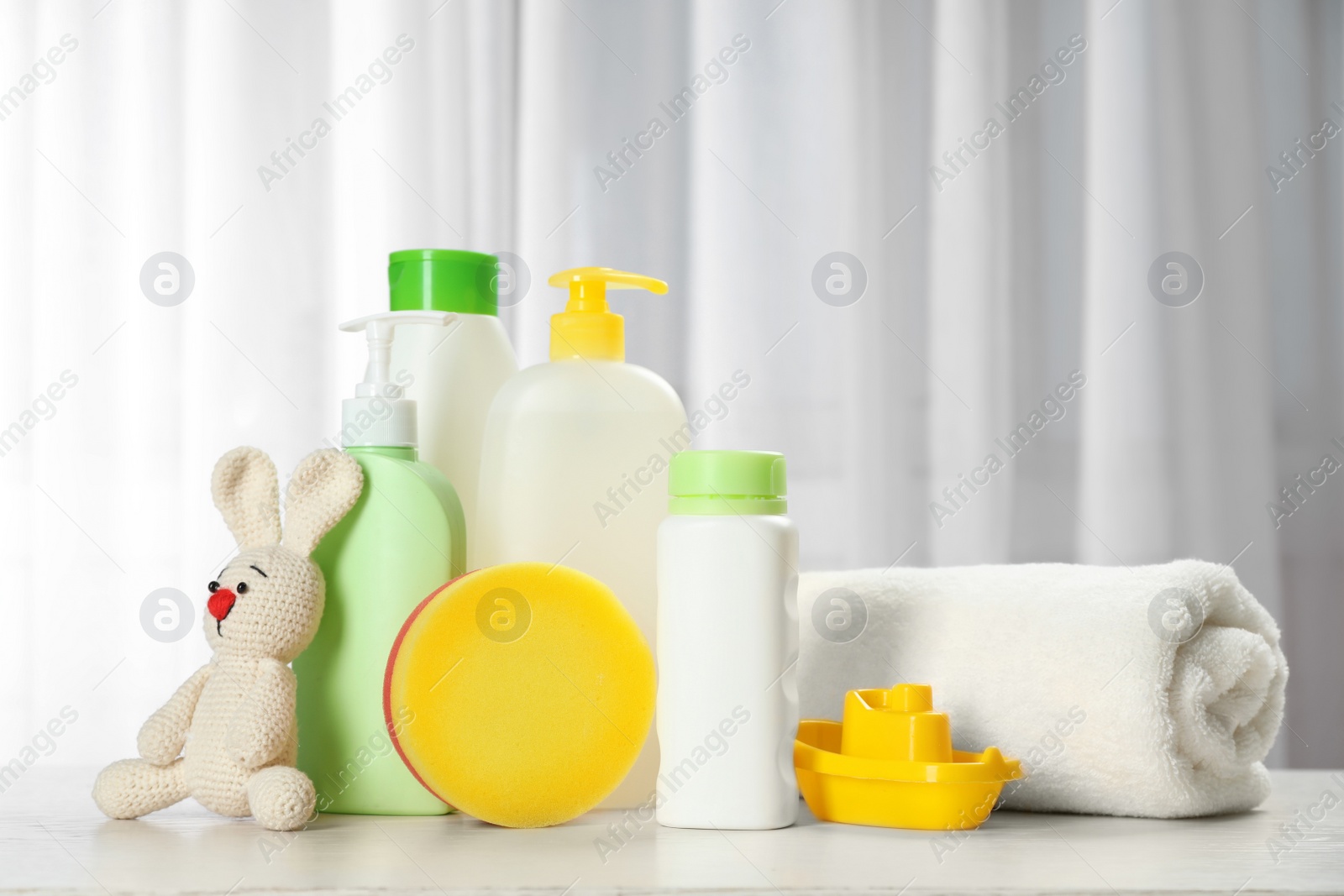 Photo of Baby cosmetic products, toys and towel on table indoors