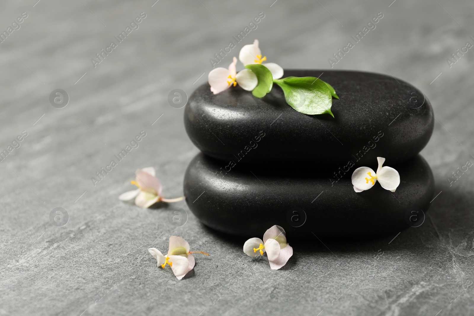 Photo of Stacked spa stones with flowers and leaves on table. Space for text