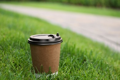 Photo of Paper cup of hot coffee on green grass outdoors, closeup with space for text. Takeaway drink