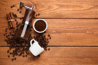 Modern manual coffee grinder with beans, powder, cup and cinnamon on wooden table, flat lay. Space for text