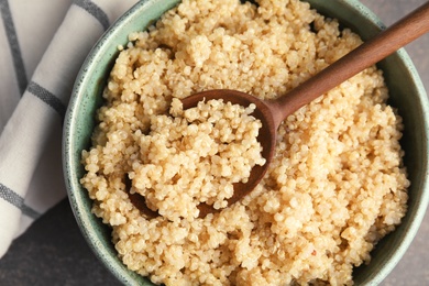 Cooked quinoa in bowl and wooden spoon on table, closeup