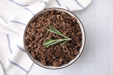 Fried ground meat in bowl and rosemary on white tiled table, top view