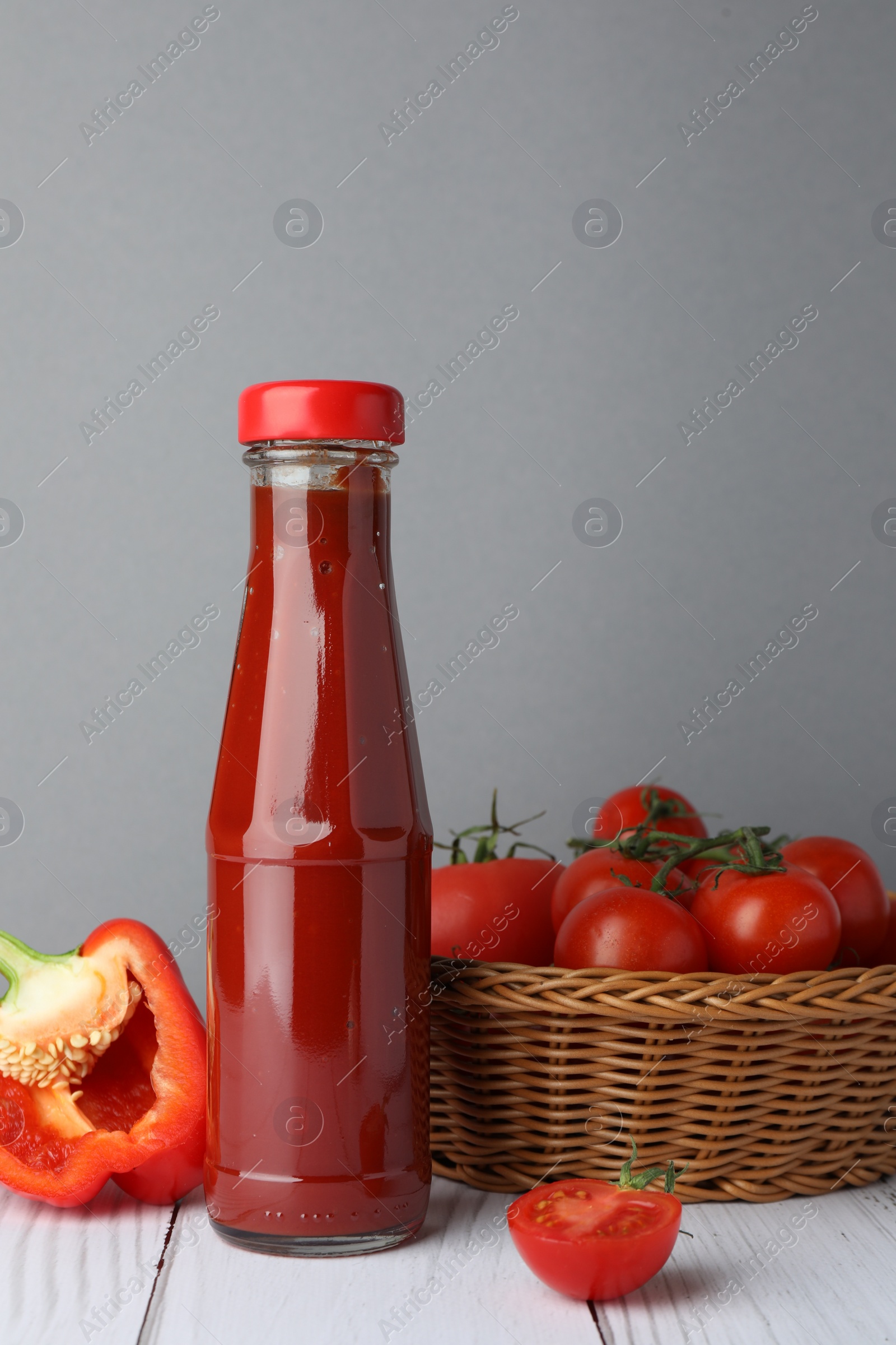 Photo of Bottle of tasty ketchup, tomatoes and pepper on white wooden table