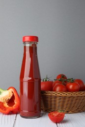 Bottle of tasty ketchup, tomatoes and pepper on white wooden table